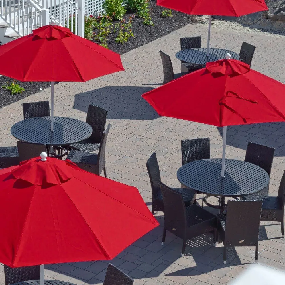 Multiple red market umbrellas shading round dining tables in a commercial outdoor patio layout